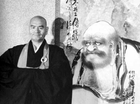 Photographie en noir et blanc du maître zen Deshimaru devant une estampe représentant Bodhidharma, un célèbre moine bouddhiste.